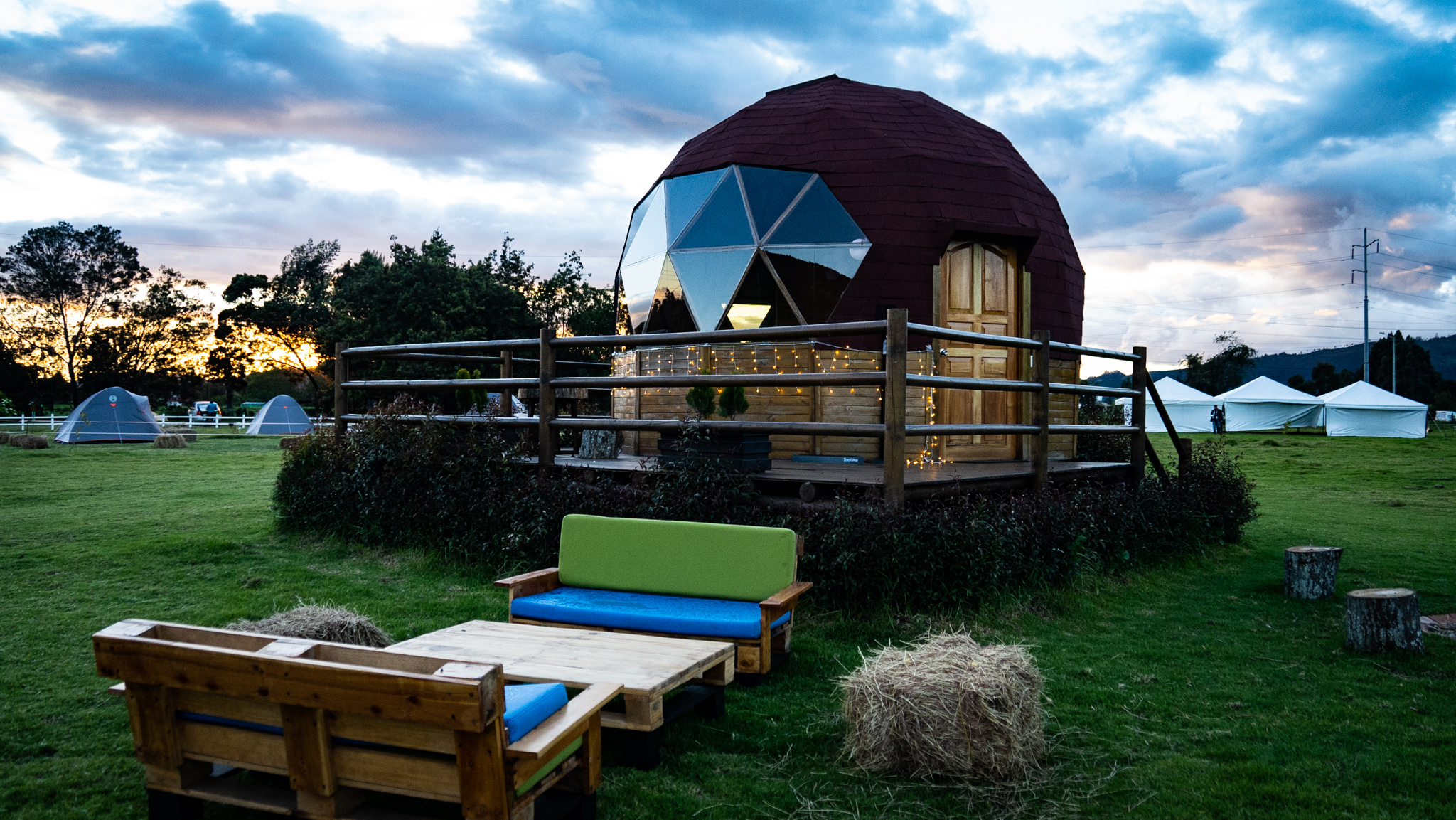 Domo glamping iluminado al atardecer en El Nodo Glamping, rodeado de naturaleza y carpas